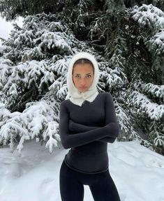 a woman standing in the snow with her arms crossed wearing a hoodie and black leggings