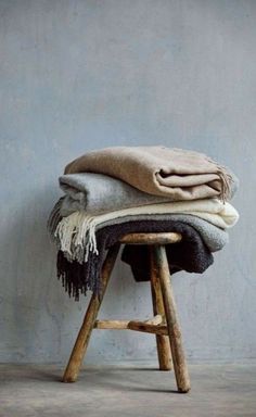 two blankets are stacked on top of a wooden stool in front of a gray wall