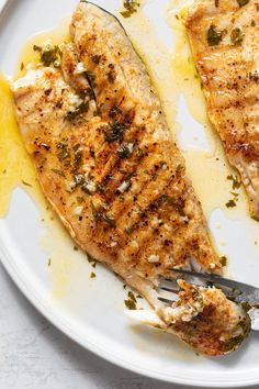 two fish fillets on a plate with lemon wedges and seasoning sprinkles