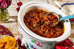 a crock pot filled with chili and meat next to other food on a table