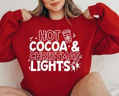 a woman wearing a red sweatshirt that says hot cocoa and christmas lights