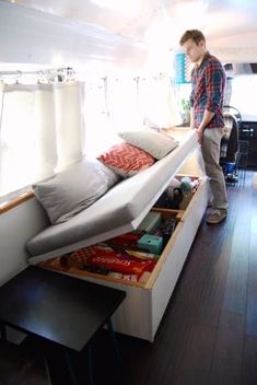 a man standing next to a bed in a room with wooden floors and white walls