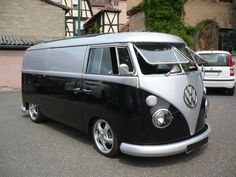 an old vw bus parked in a parking lot next to other cars and buildings