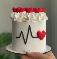 a hand holding a cake with white frosting and red hearts