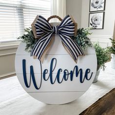 a welcome sign with a bow on it sitting on top of a table next to a potted plant