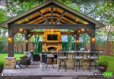 an outdoor kitchen with bar stools under a covered grill and seating area in the back yard