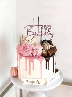 a birthday cake with pink and white icing on a table in front of a wall