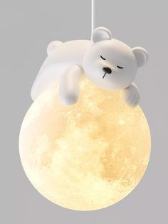 a white teddy bear hanging from a string with the moon in the sky behind it