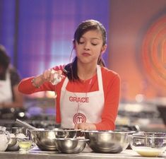 a woman in an orange and white shirt is cooking food on a table with bowls