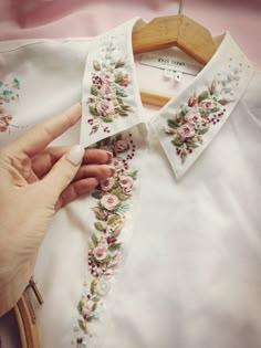 a woman's hand touching the collar of a white shirt with flowers on it