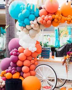 an assortment of balloons are hanging from the ceiling in front of a cart full of pumpkins