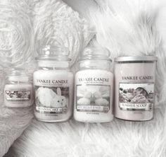 three yankee candles sitting next to each other on a white fur covered surface with a teddy bear in the background