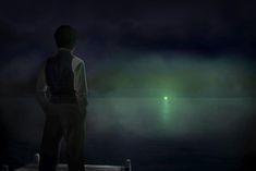 a man standing on a dock looking at the water with a green light in the distance