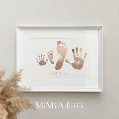 a white frame with two hand and foot prints on it next to a potted plant