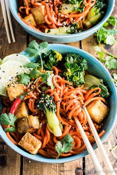 two bowls filled with noodles, broccoli and tofu in red curry sauce