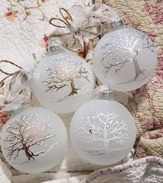 four white glass ornaments with tree designs on them sitting on a quilted tablecloth