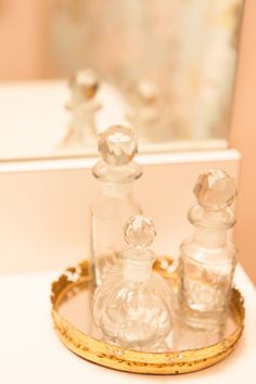 two glass bottles sitting on top of a white table next to a mirror and gold rimmed tray