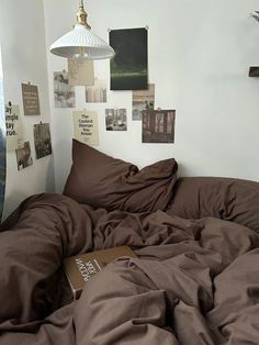 an unmade bed with brown sheets and pictures on the wall next to it in a bedroom