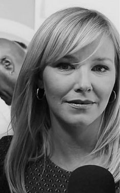 a black and white photo of a woman talking into a microphone with a man in the background