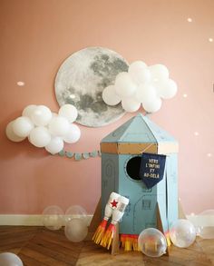 a room with balloons and a blue house on the floor in front of a pink wall