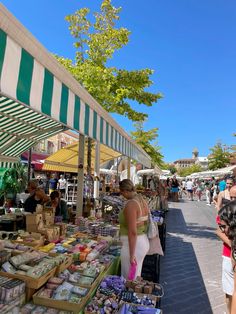 people are shopping at an outdoor market on a sunny day with green and white striped awnings