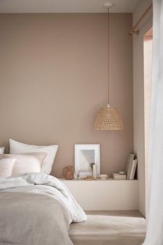 a white bed sitting next to a window with curtains on the side and a lamp hanging above it