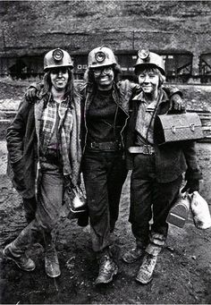 black and white photograph of three women in hard hats, one holding a suitcase while the other is carrying a dog