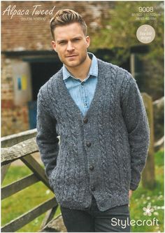 a man standing next to a wooden fence wearing a blue cardigan sweater and jeans