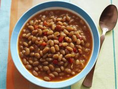 a blue bowl filled with beans on top of a table next to a silver spoon