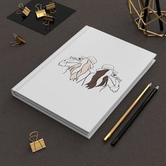 an open notebook sitting on top of a table next to pencils and paper clips