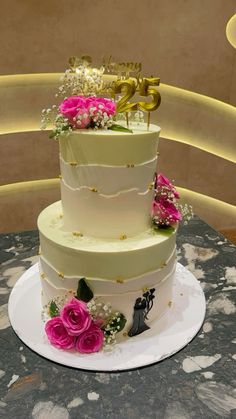 a three tiered wedding cake with flowers on the side and gold numbers on top