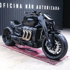 a black motorcycle parked on top of a red rug in front of a metal wall