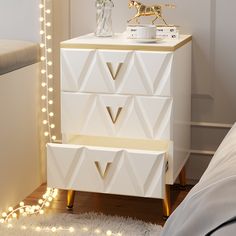 a white and gold dresser with lights on the wall next to it in a bedroom