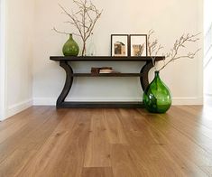 two green vases sitting on top of a wooden table next to a shelf filled with books