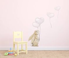 a bunny holding balloons in the air next to a wooden chair and wall decal