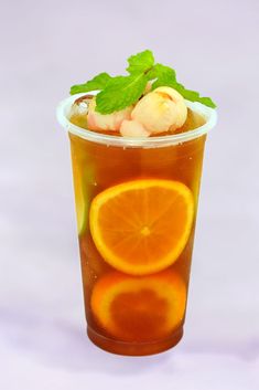 a cup filled with liquid next to an orange slice and mint sprig on top