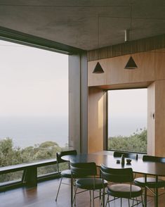 a dining room table with four chairs next to a large window overlooking the ocean and trees