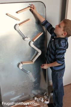 a little boy that is standing in front of a metal wall with pipes on it