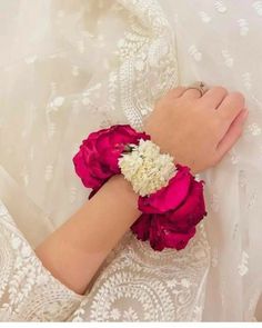 a woman's arm wearing a white and red flower bracelet on top of a bed