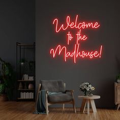 a welcome to the madhouse neon sign in a dark room with a chair and table