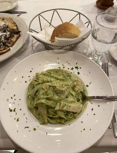 there is a plate of pasta with pesto sauce on it and bread in the background