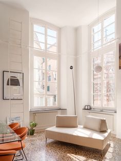 a living room filled with furniture next to two large windows on top of a tiled floor