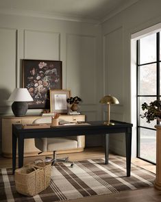 a room with a desk, lamp and pictures on the wall next to large windows