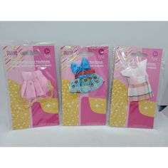 three packaged dolls in plastic packaging on a white tablecloth with pink and yellow polka dots