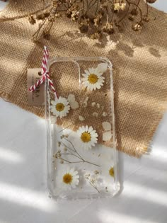 an iphone case with daisies on it sitting next to a straw and some flowers