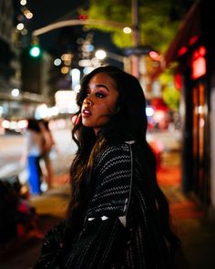 a woman is standing on the sidewalk at night with her eyes closed and long hair flowing in the wind