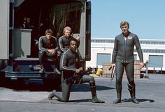 five men in wetsuits standing next to a truck