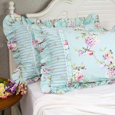 a white bed topped with lots of pillows next to a wooden table and flowers on it