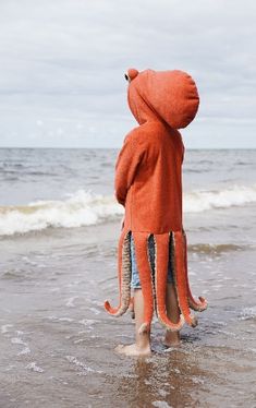 an octopus stuffed animal standing in the water at the beach with its head sticking out