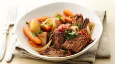 a white bowl filled with meat, vegetables and carrots on top of a table